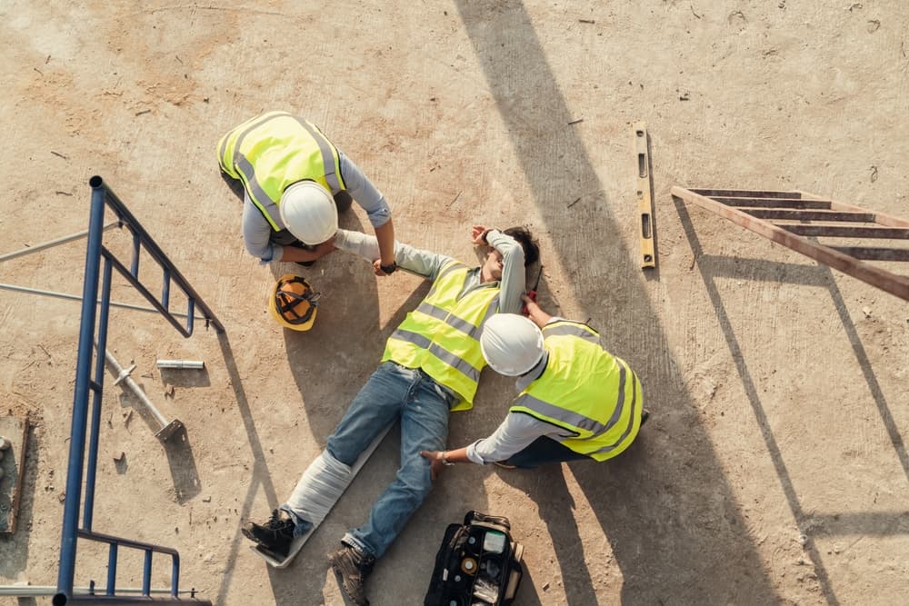A builder falls from scaffolding onto a concrete floor, resulting in an accident. The safety team assists the employee, who has sustained arm and leg injuries.