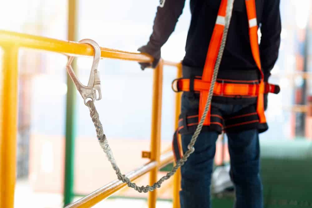 A construction worker using a safety harness and safety line while working on a new construction site project.
