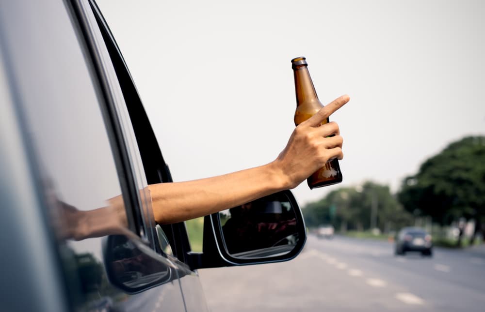The image of a man's hand holding a jar of alcohol while driving, representing driving negligence.